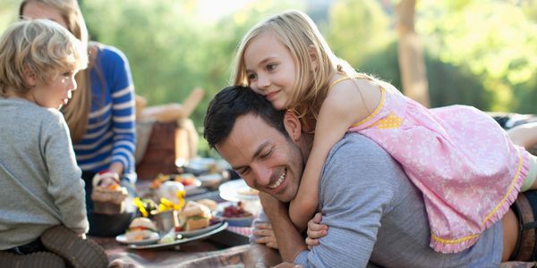 A little girl hugs a smiling man during a picnic with family outdoors.