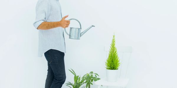 Man watering plants indoors with a metal watering can.