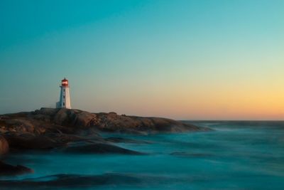 A peaceful scene of a lighthouse at sunrise, surrounded by calm water and blue sky.