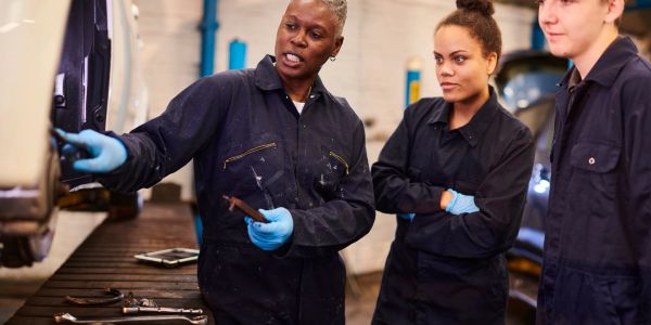 Instructor teaching auto repair to two students.