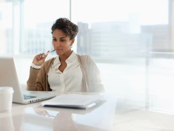 Femme réfléchissant devant un ordinateur portable.