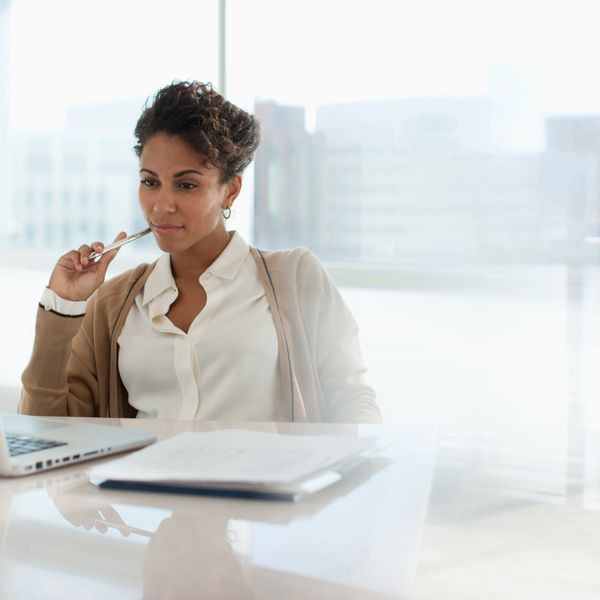 Woman thoughtfully working on a laptop in a bright office.