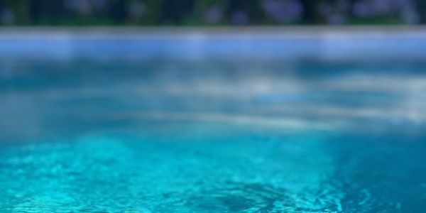 Close-up of clear blue water in a pool with blurred greenery in the background.