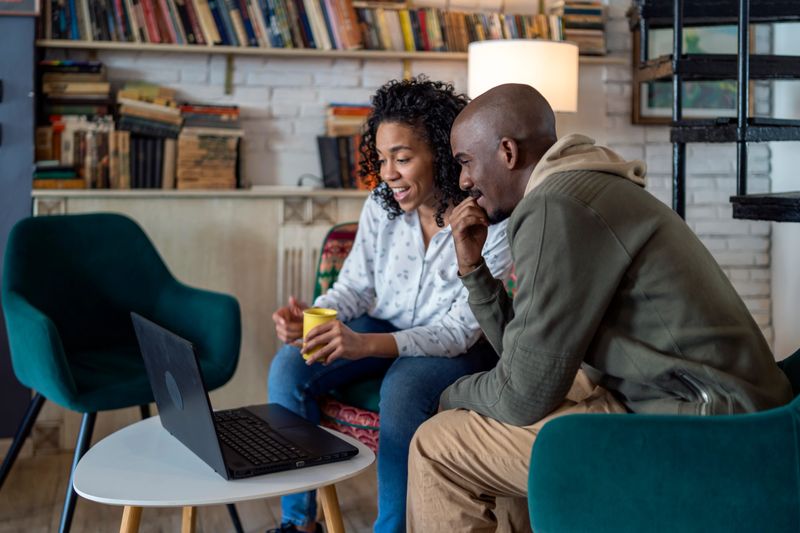Afro couple at home using laptop and talking.