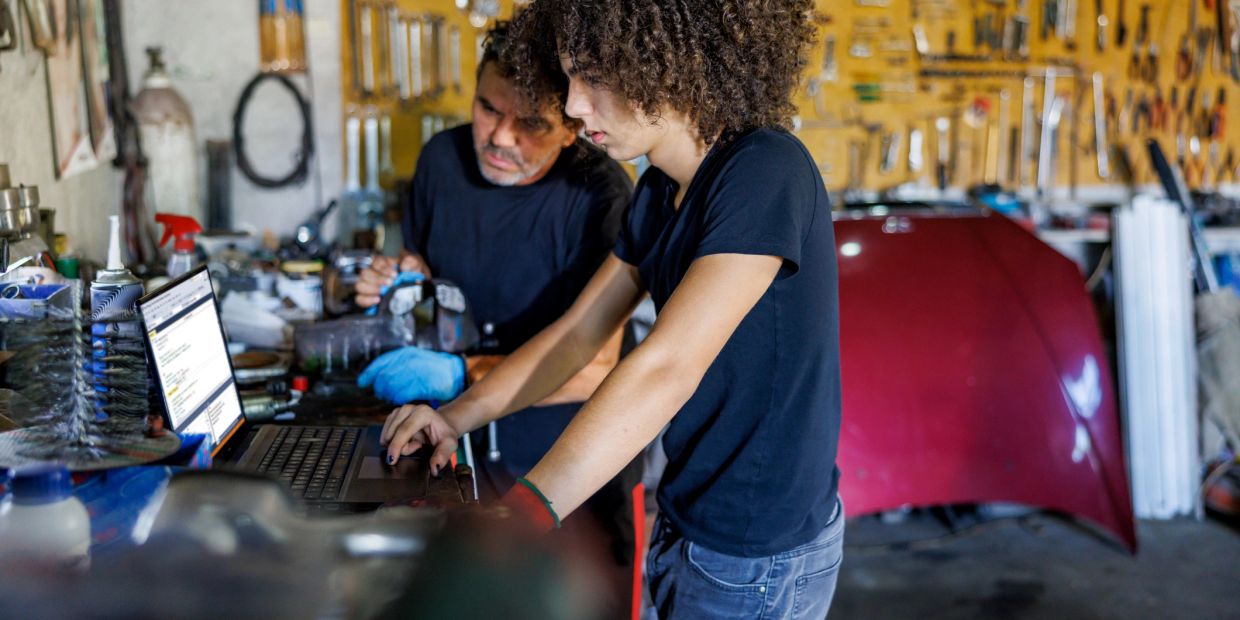 Two mechanics working on a laptop in a garage.