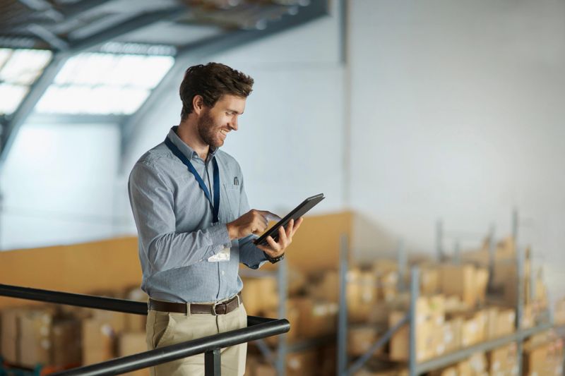 Man, tablet and warehouse manager with inventory of boxes for delivery, export or email for orders in ecommerce. Smile, logistics and employee with digital app for online stock checklist in storage.