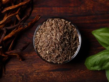Bowl of cumin seeds on wooden surface.