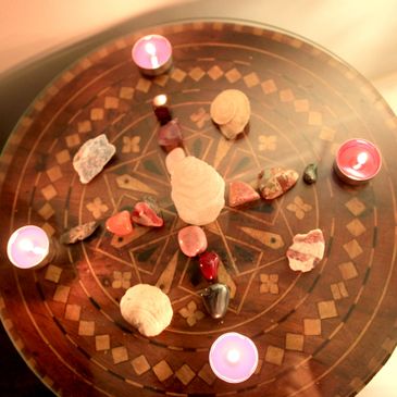 Decorative table with crystals, seashells, and lit candles arranged in a circle.