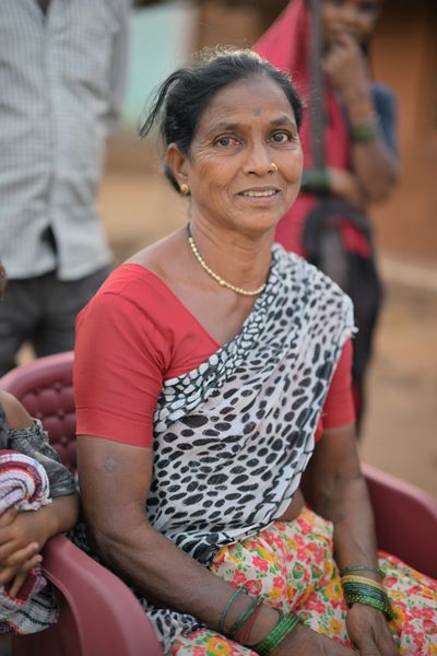 Smiling woman in a patterned sari sitting outdoors.