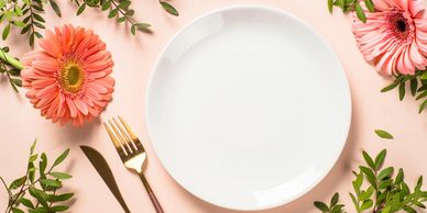 Empty white plate with gold cutlery and flowers.