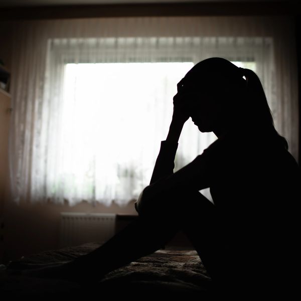Silhouette of a person sitting with head in hand, appearing stressed or contemplative.