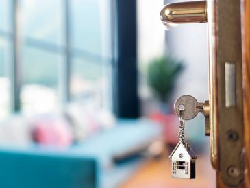 Key with a house-shaped keychain in a door lock of a cozy living room.