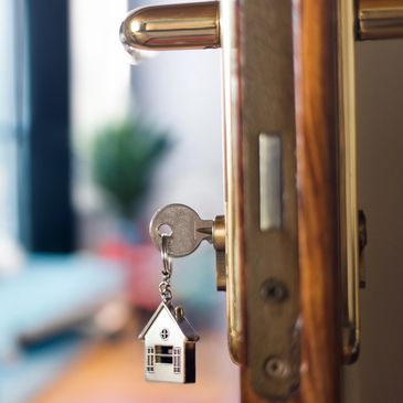 Key with a house-shaped keychain inserted in a door lock.