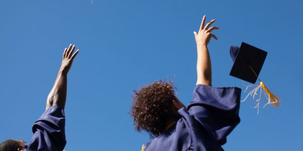 Graduates in caps and gowns throw their hats in the air against a clear blue sky.