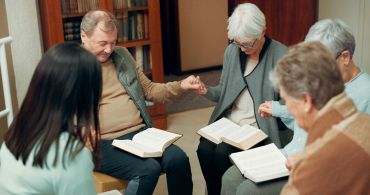 Group of elderly people holding hands and praying together.