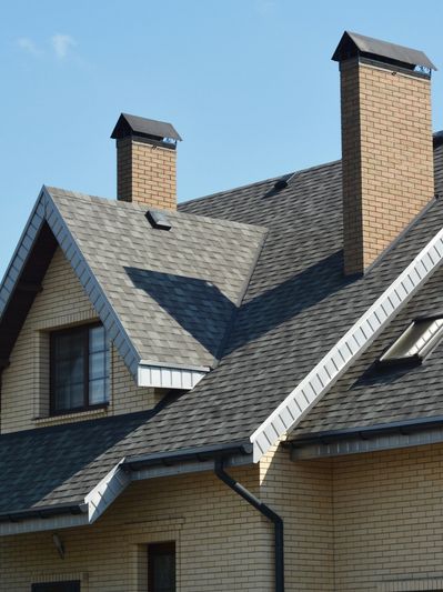 Modern house with a gray shingled roof and brick walls under a clear blue sky.