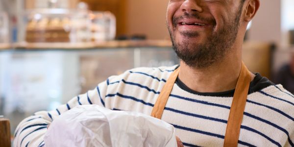 Smiling man in striped sweater and apron holding a wrapped item.