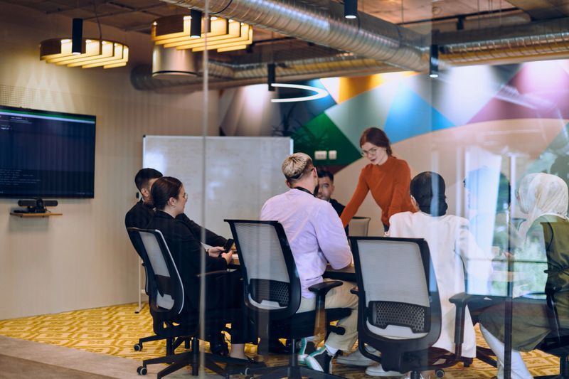 A diverse team of business experts in a modern glass office, attentively listening to a colleague's presentation, fostering collaboration and innovation
