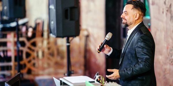 Man speaking into a microphone at an indoor event.