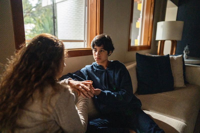 Mother giving advice and holding son's hand at home