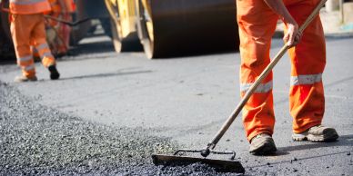 Workers in orange uniforms paving a road with asphalt.