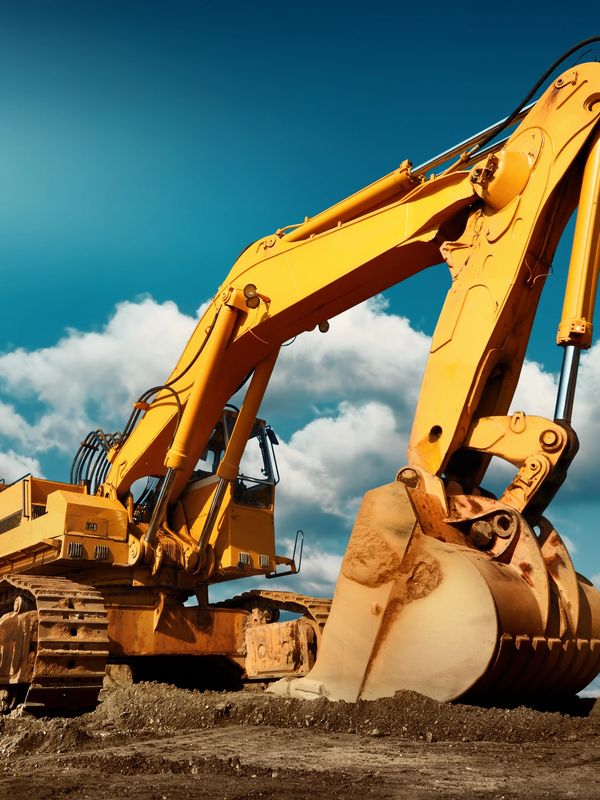 Yellow excavator at a construction site with blue sky and clouds.