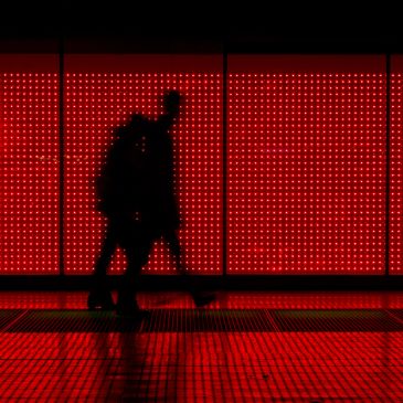Silhouetted figure walking past a vibrant red LED-lit wall at night.