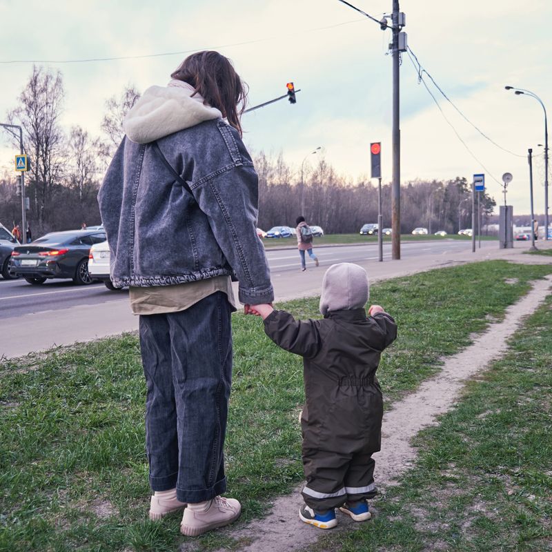 The boy and his mother walk along the city street, observing the passing cars.