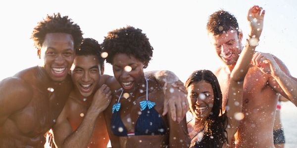 A group of five friends laughing and splashing water at the beach.