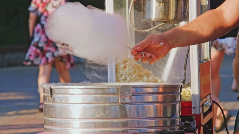 Caucasian Man Perparing Sweet Sugar Candyfloss on Outdoor Stand by Crowded Boulevard