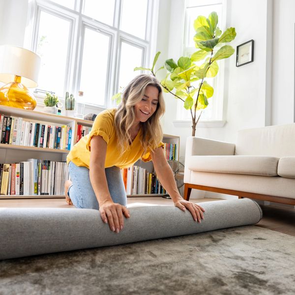 Woman rolling up a gray rug in a sunny living room.