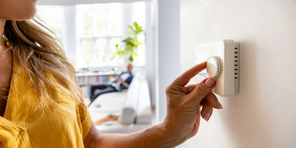 Woman adjusting the thermostat in a bright living room.