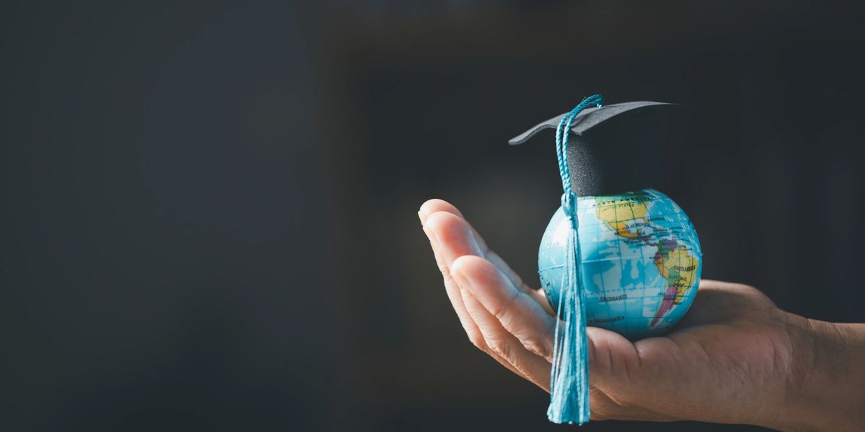 Hand holding a globe with a graduation cap symbolizing global education.