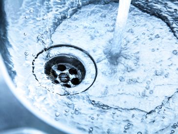 Close-up of water flowing into a stainless steel sink drain.