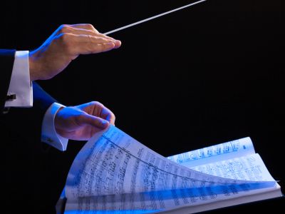 Conductor leading with baton and sheet music.