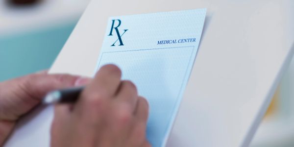 Person writing a prescription on a medical center pad.