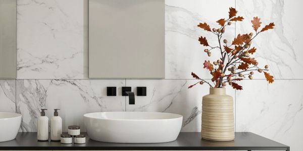 Modern bathroom with marble walls, black countertop, and autumnal vase decor.
