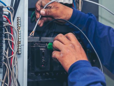 Electrician working with wires inside an electrical panel.