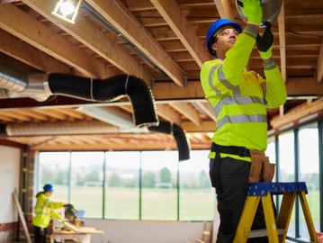 Worker installing ductwork indoors on a ladder.