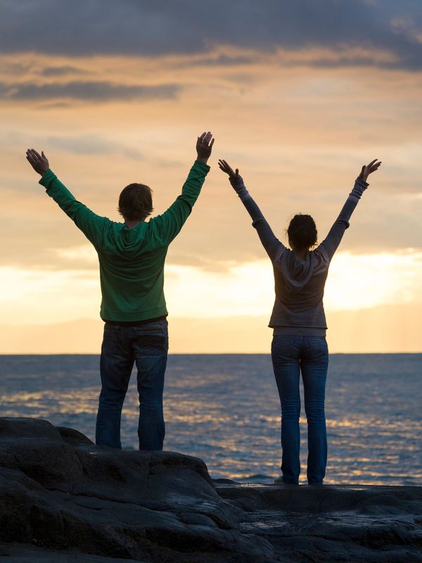 Two people with raised arms enjoying a sunset by the sea.