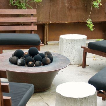 Outdoor seating area with black cushions and a modern fire pit with decorative black spheres.