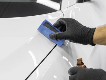 Person applying a protective coating to a white car's surface.