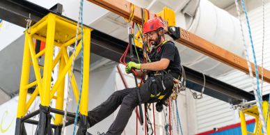 Man in safety gear working on ropes indoors.