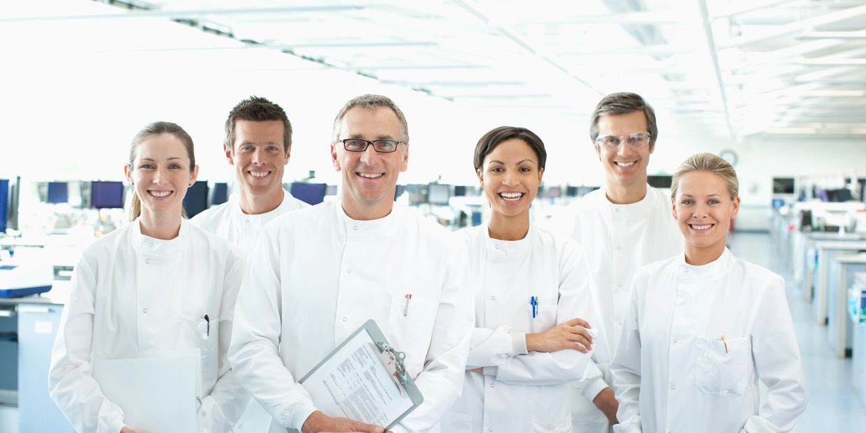 Group of six scientists in lab coats smiling.