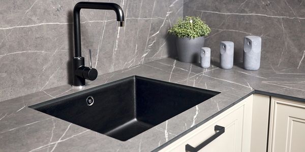 Modern kitchen sink with black faucet and gray marble countertop.