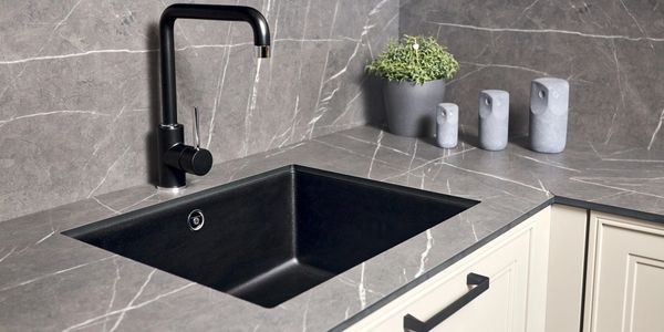 Modern kitchen sink with black faucet and gray marble countertop.