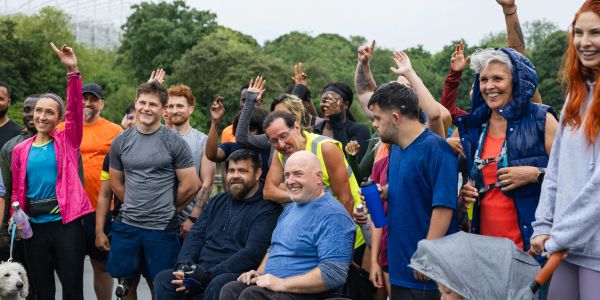 Diverse group of people smiling and raising hands outdoors, including a man in a wheelchair.