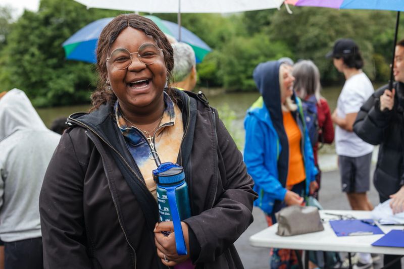 Group of run participants taking part in a fun run in Leazes Park in Newcastle upon Tyne in the North East of England. They are ready to run in the rain along the lakeside. The race is open to people of all ages and abilities and is also dog friendly. A woman is laughing looking at the camera holding a water bottle.