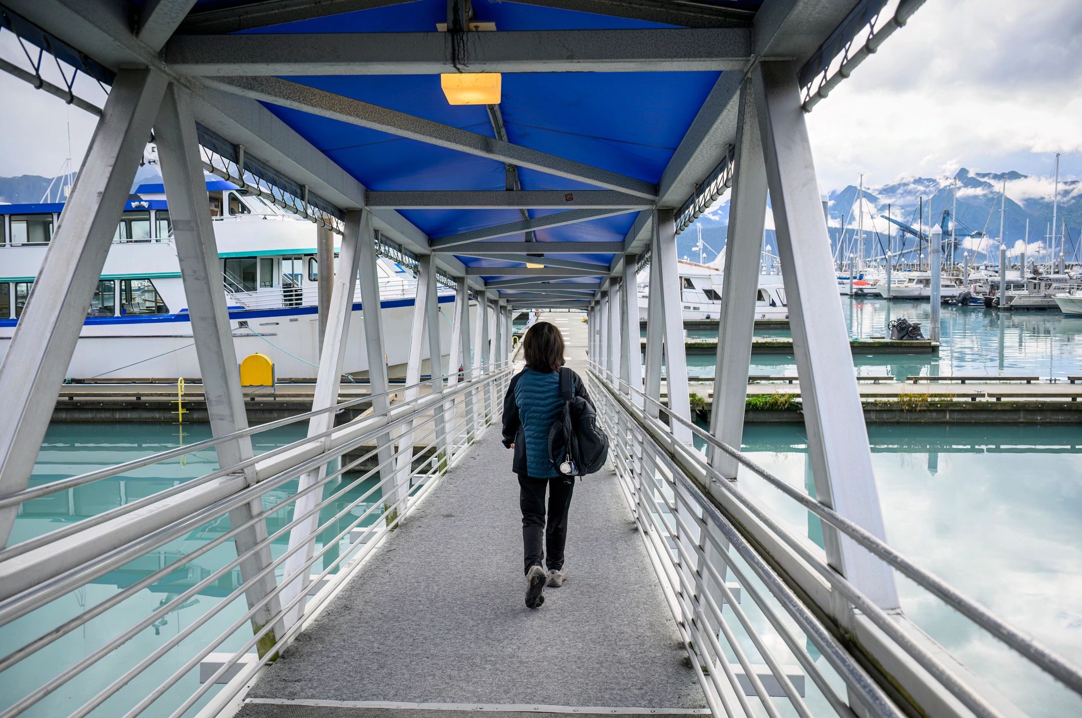 A person walking onto the deck of an Alaska ocean cruise ship with snowy mountain in the background.