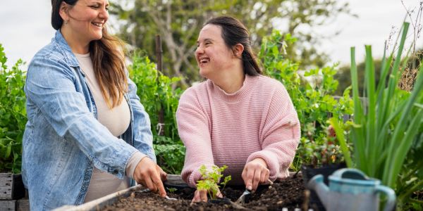 Two women happily gardening together in a green garden bed.